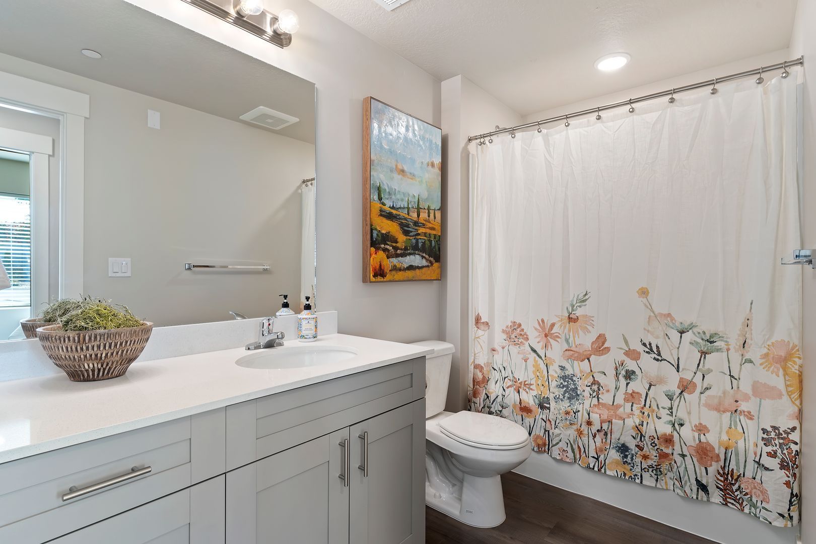 Bathroom with light gray cabinets, white countertop, and floral shower curtain.