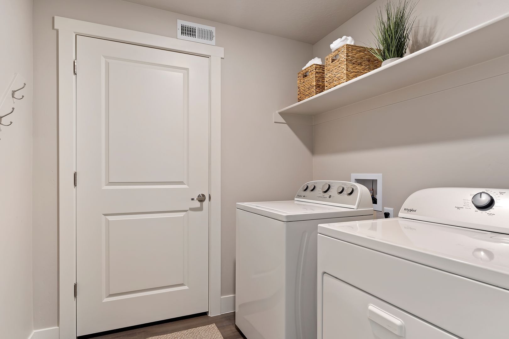 Laundry room with white washer and dryer, door, and shelf with baskets and plant.