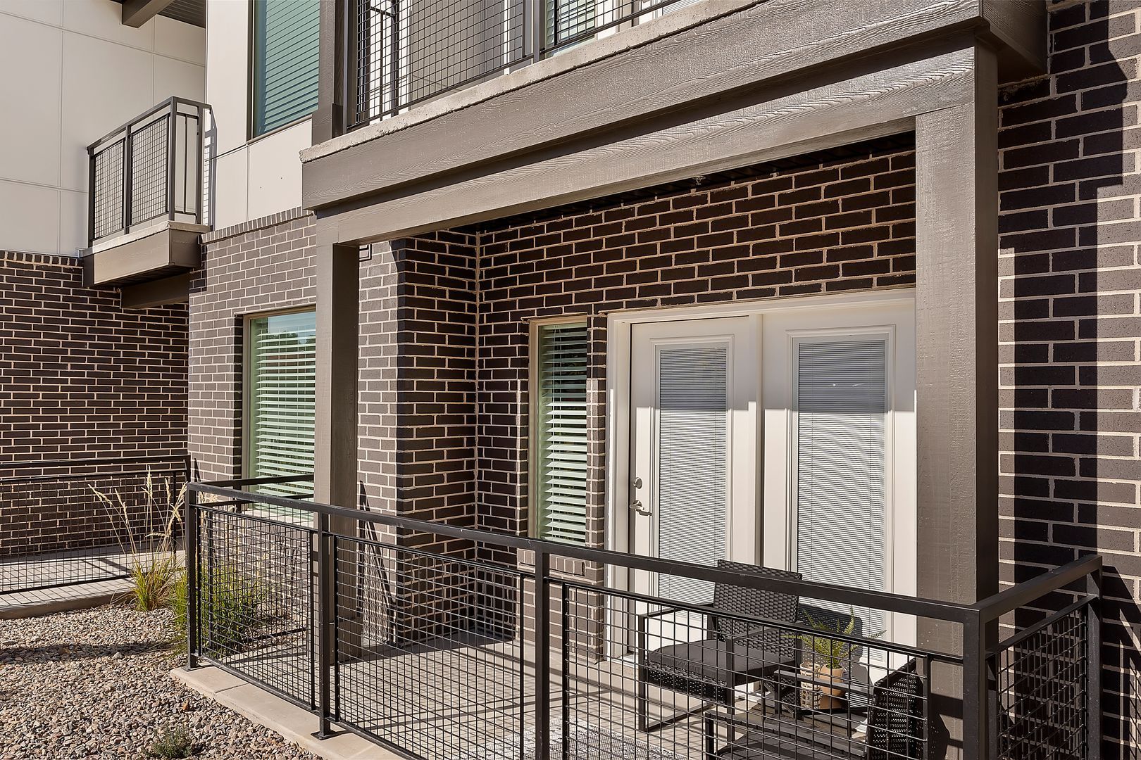 Balcony with black metal railing and chairs; brick wall and white double doors.