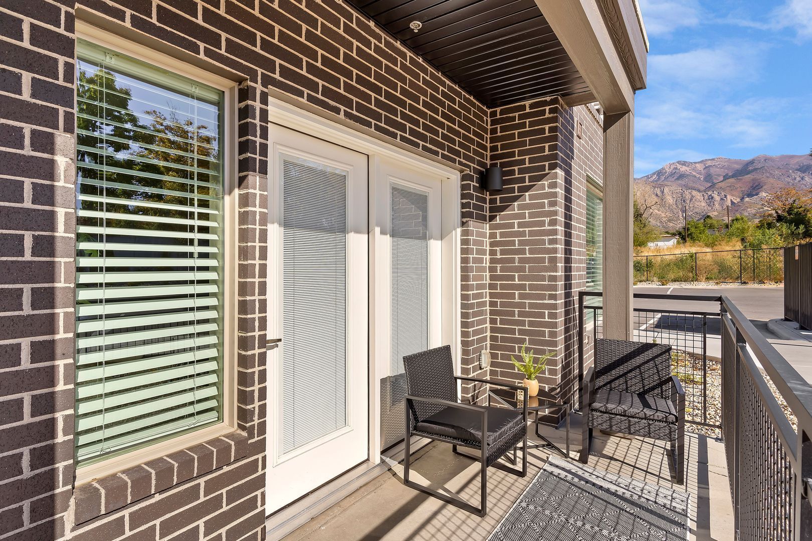 Balcony with brick wall, white doors, black chairs, and mountain view.