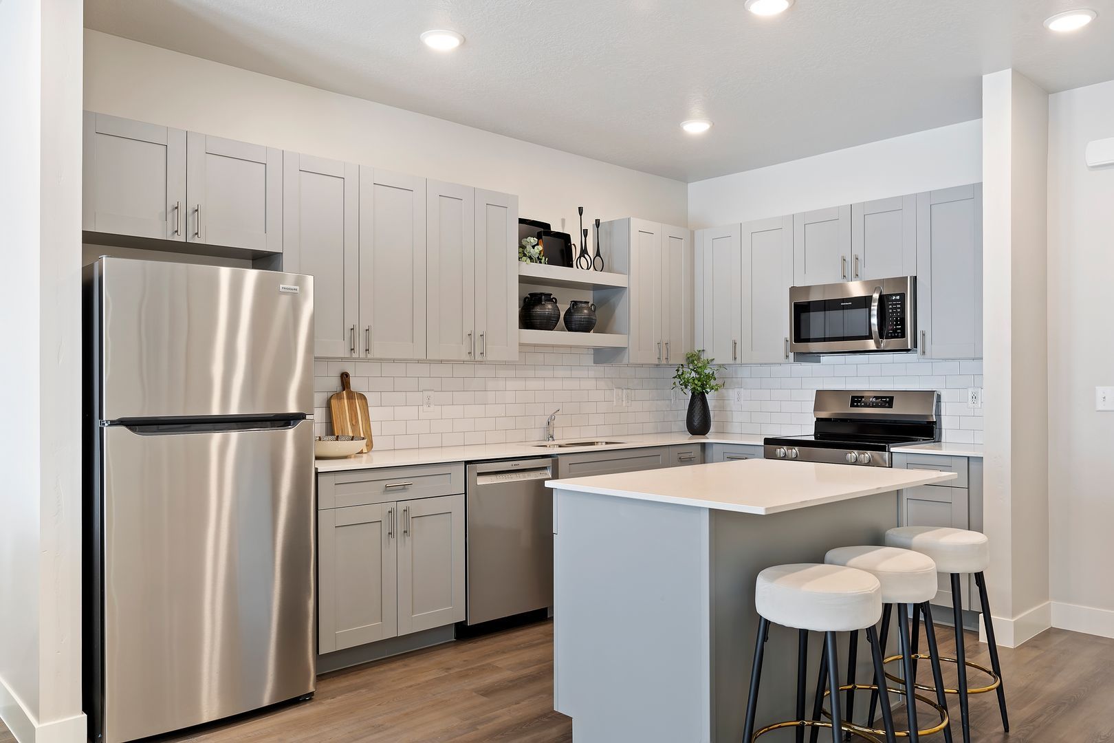Modern kitchen with gray cabinets, stainless steel appliances, and a white island with stools.