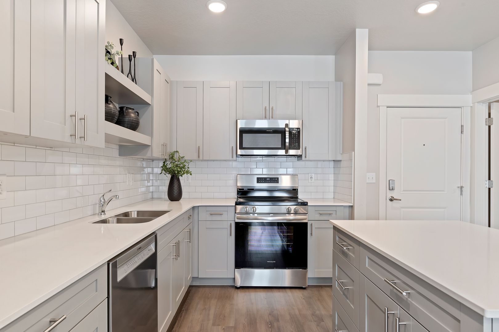 A modern kitchen with gray cabinets, white countertops, stainless steel appliances, and wood flooring.