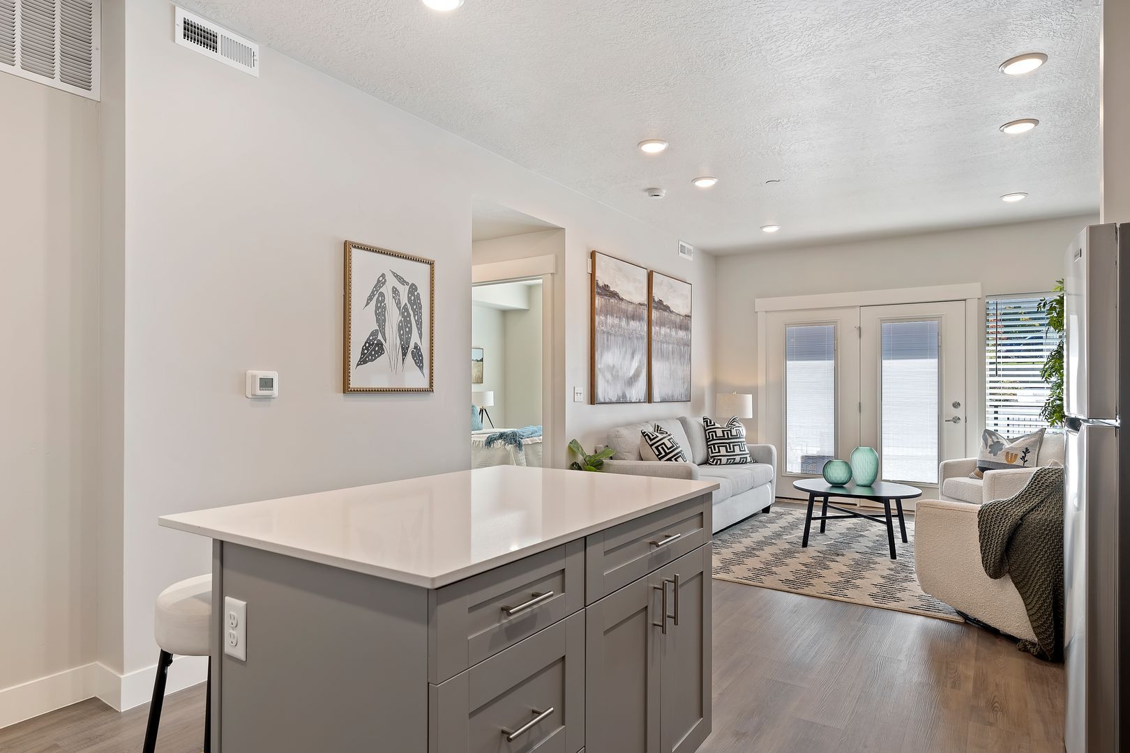 Kitchen island and open-concept living area with light-colored walls, sofa, and French doors leading to a balcony.