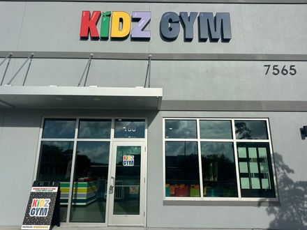 Kidz Gym storefront with colorful sign, awning, windows, and parking area.