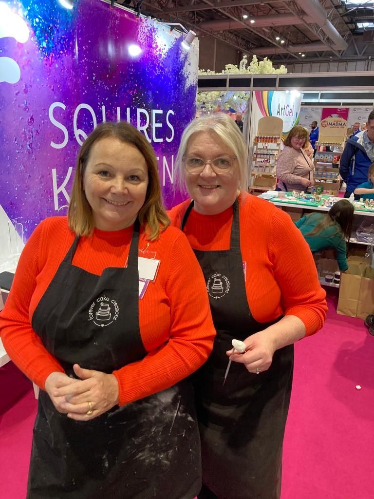 Two women wearing aprons are posing for a picture at a convention.