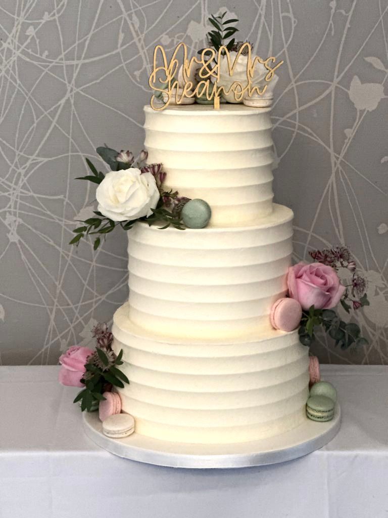 A white wedding cake with flowers and macarons on a table.