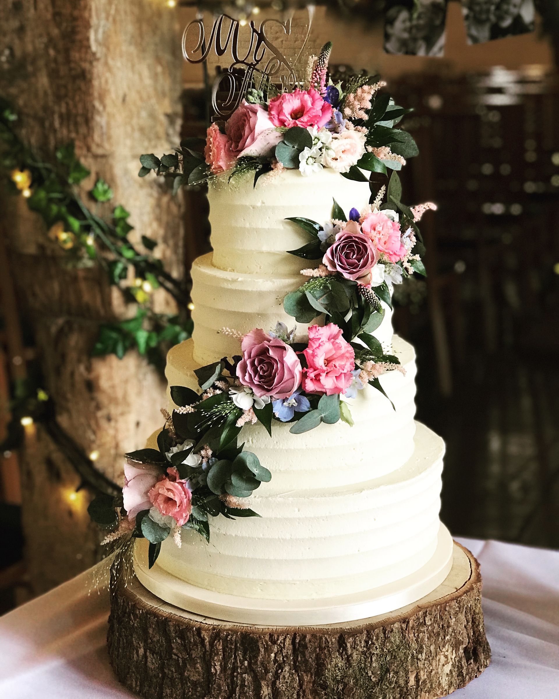 A wedding cake is sitting on top of a wooden stump on a table.
