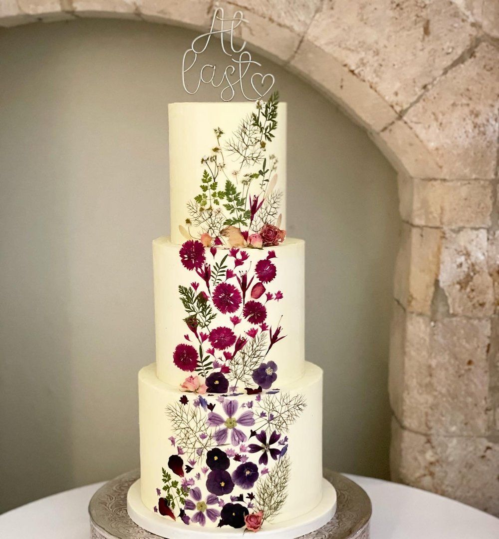 A white wedding cake with purple flowers on it