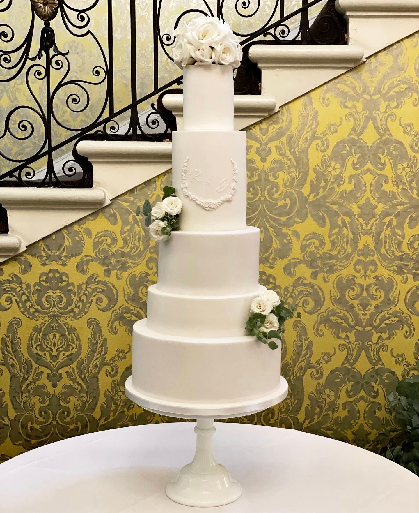 A white wedding cake is sitting on a table in front of stairs.