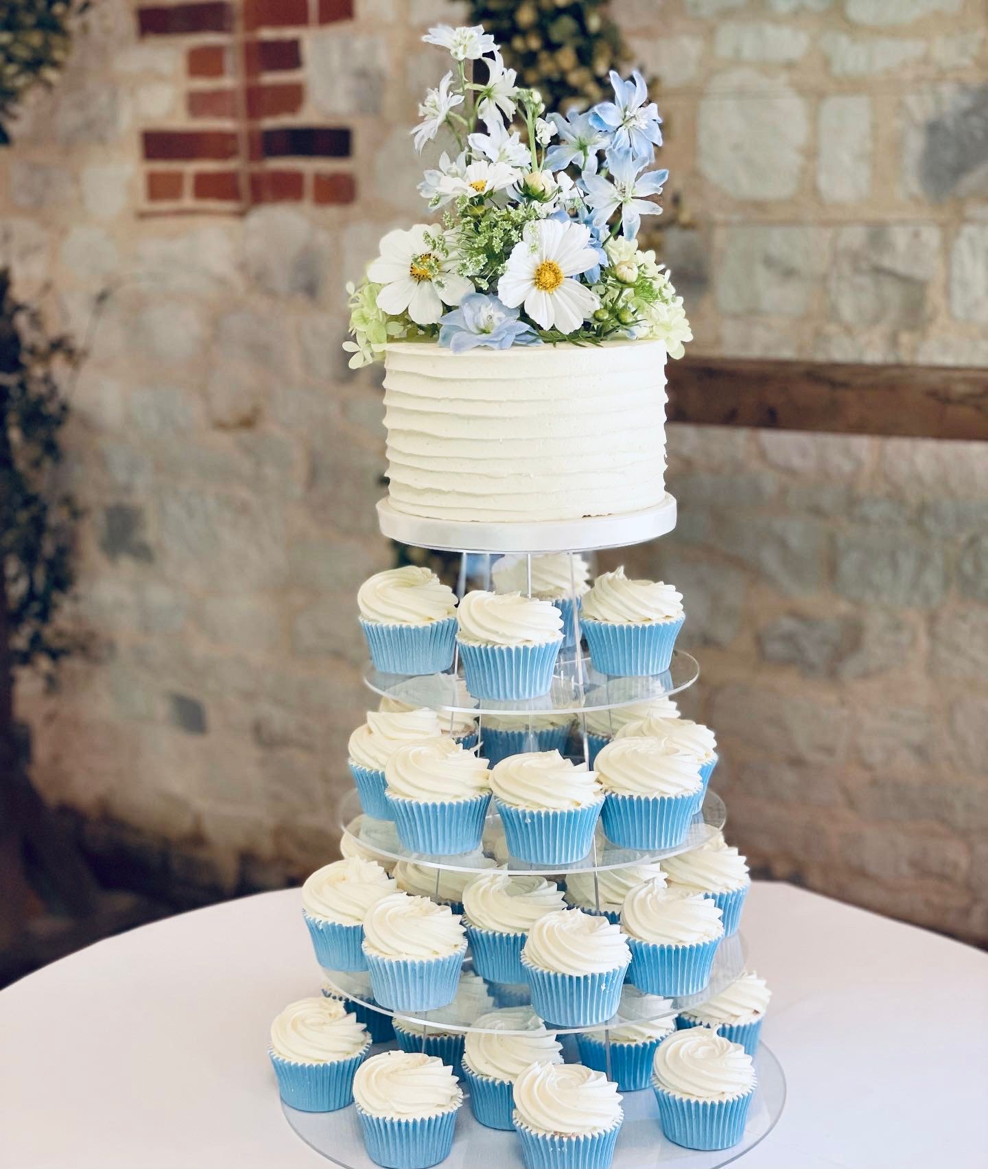 A wedding cake surrounded by cupcakes on a table.