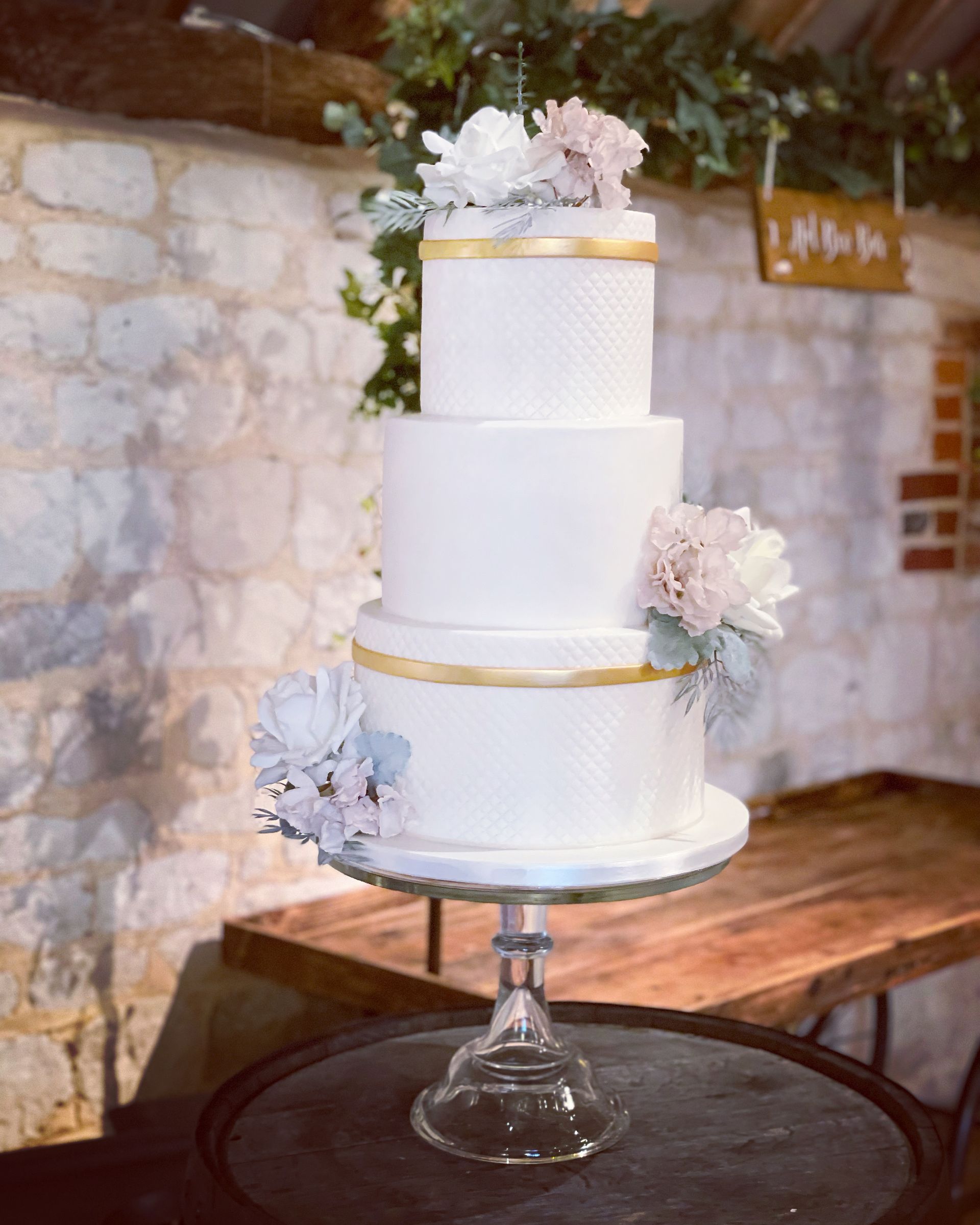 A white wedding cake is sitting on top of a glass cake stand on a table.