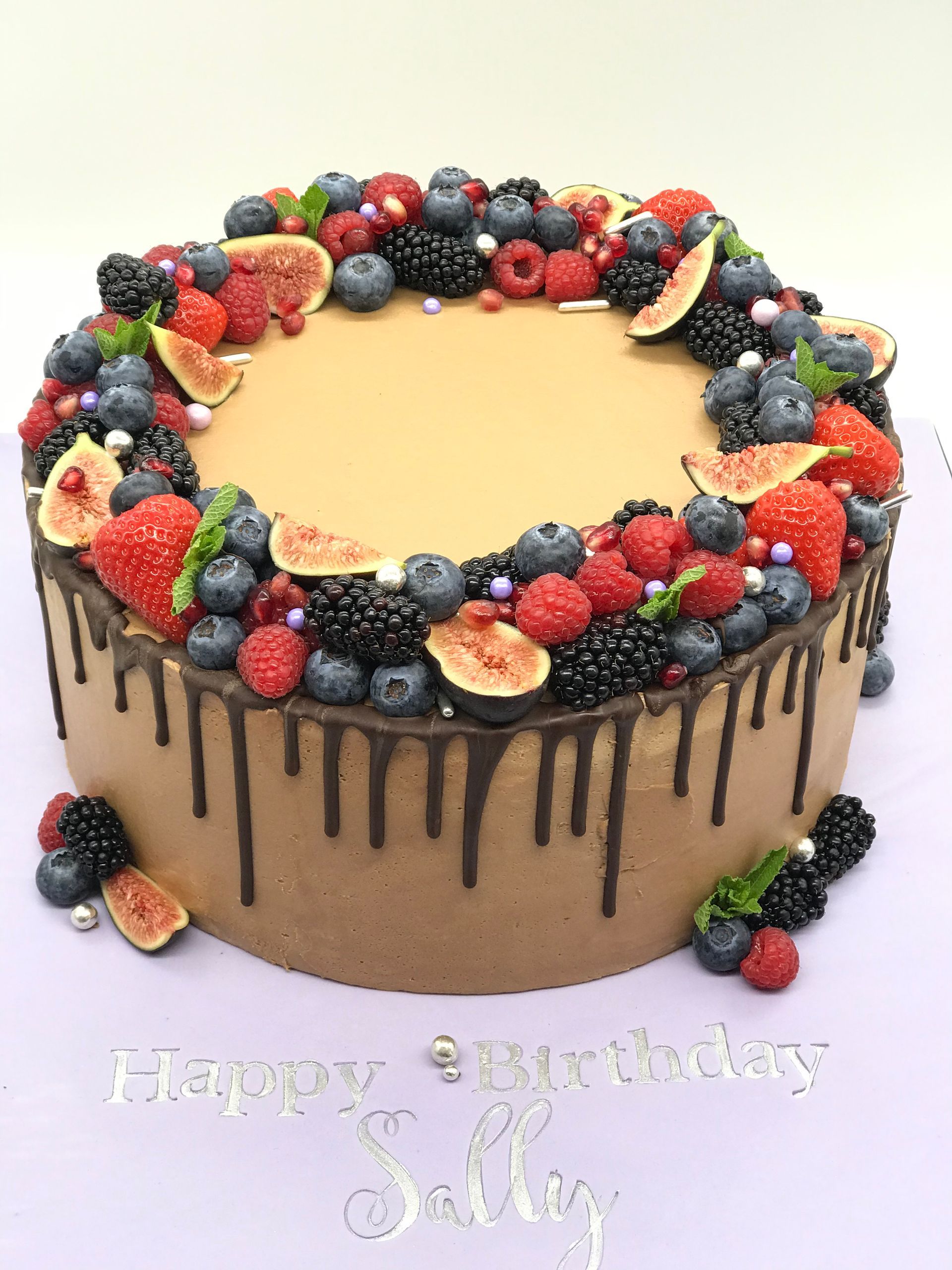 A birthday cake with chocolate drip and berries on top.