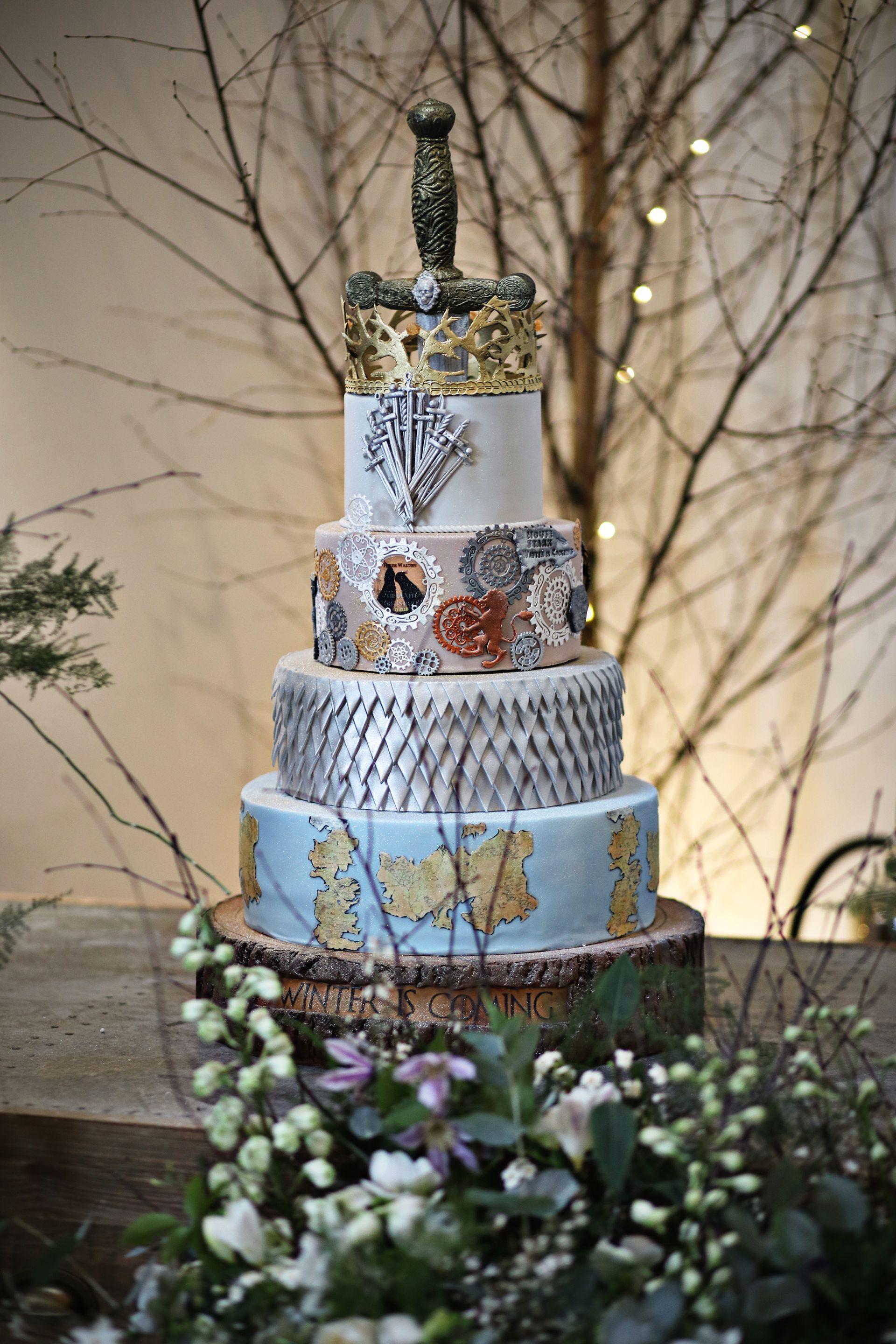 A wedding cake is sitting on top of a wooden table surrounded by flowers.