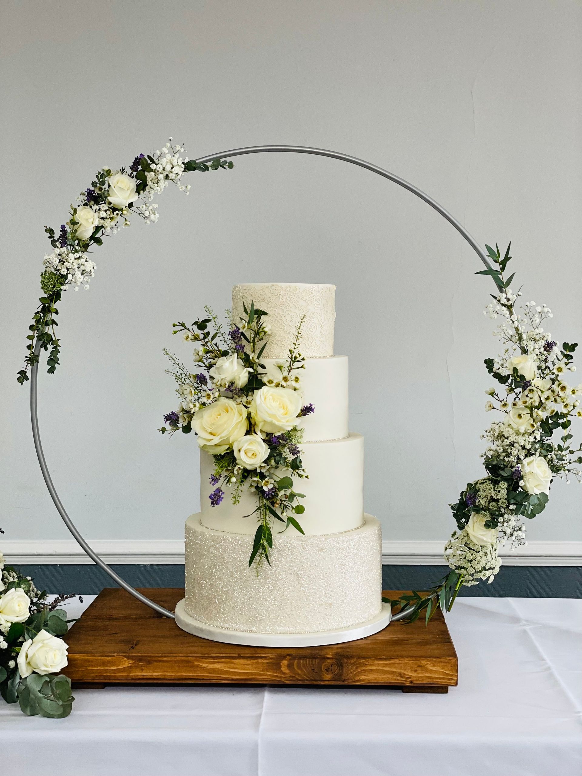 A wedding cake is sitting on top of a wooden table surrounded by flowers.