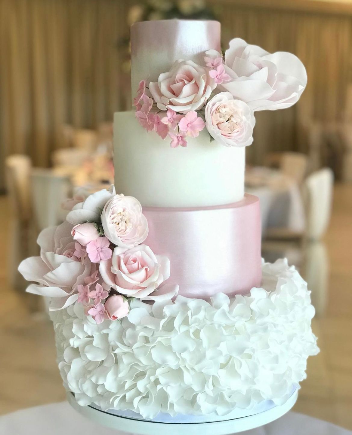 A pink and white wedding cake with ruffles and flowers on it.