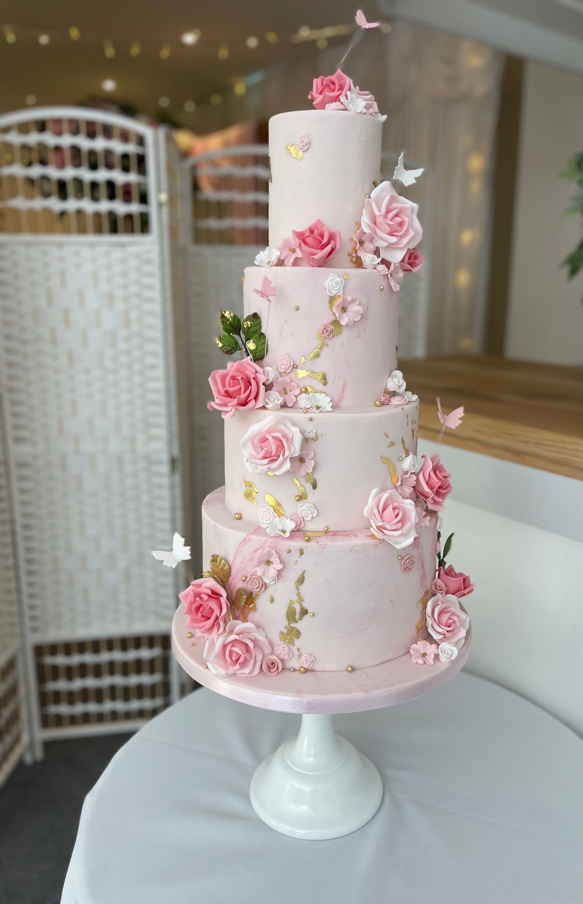 A pink wedding cake with pink roses and butterflies is sitting on a white table.