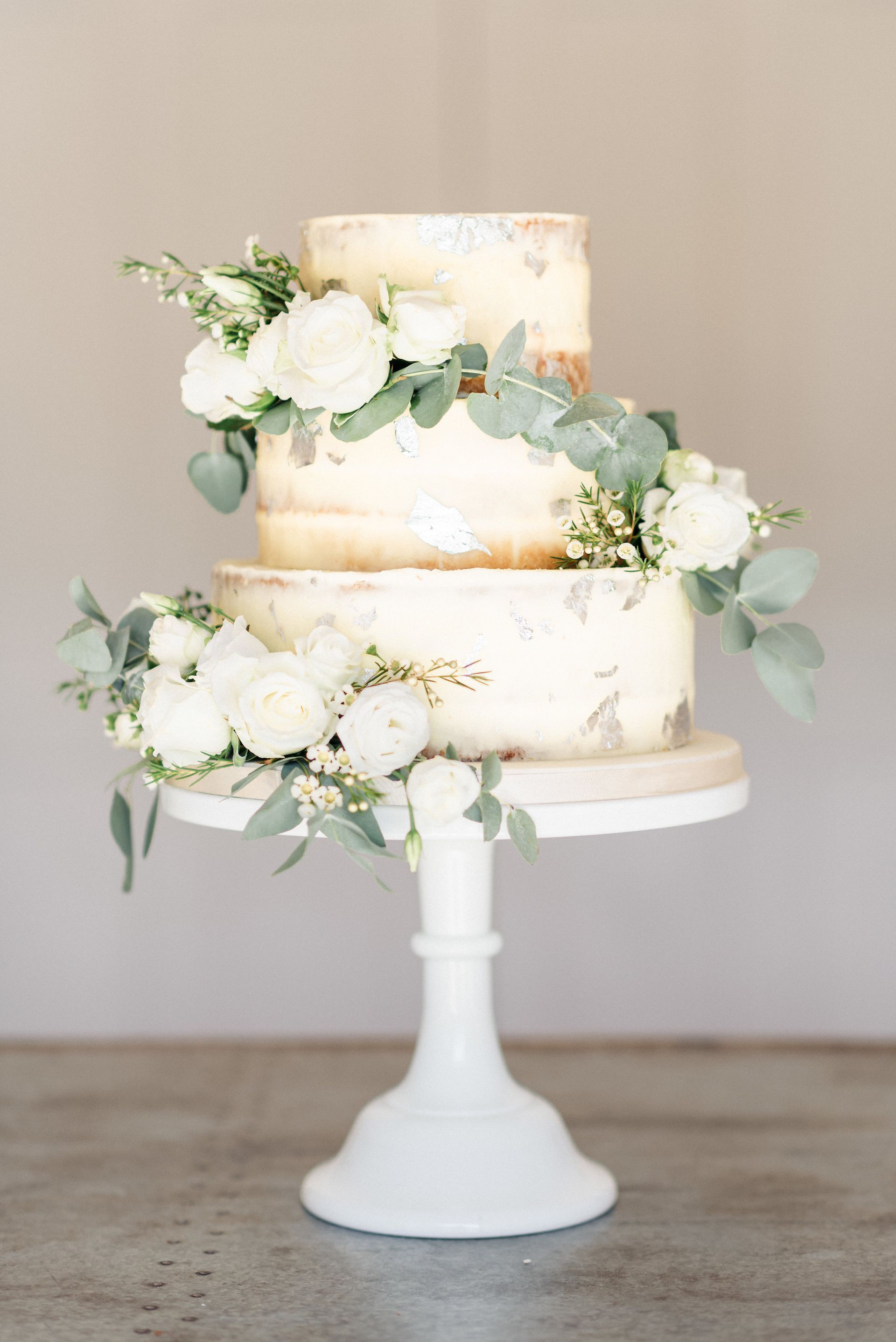 A wedding cake is sitting on top of a white cake stand.