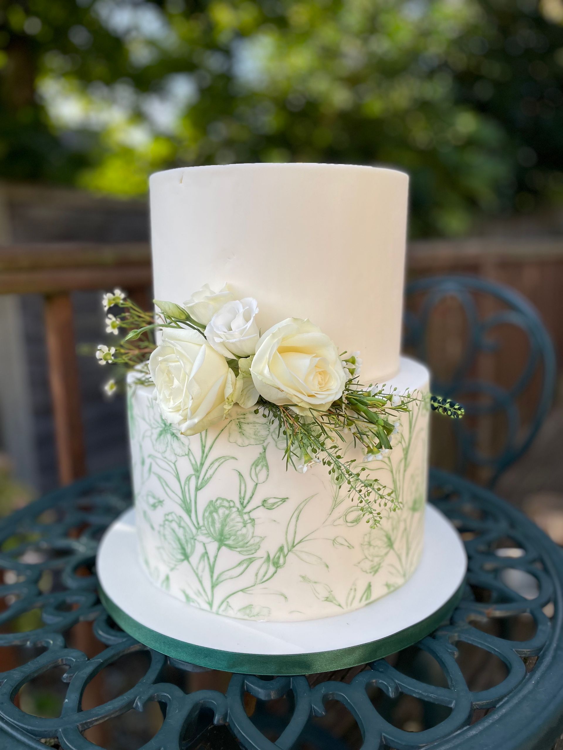 A wedding cake with white roses and green leaves is sitting on a table.