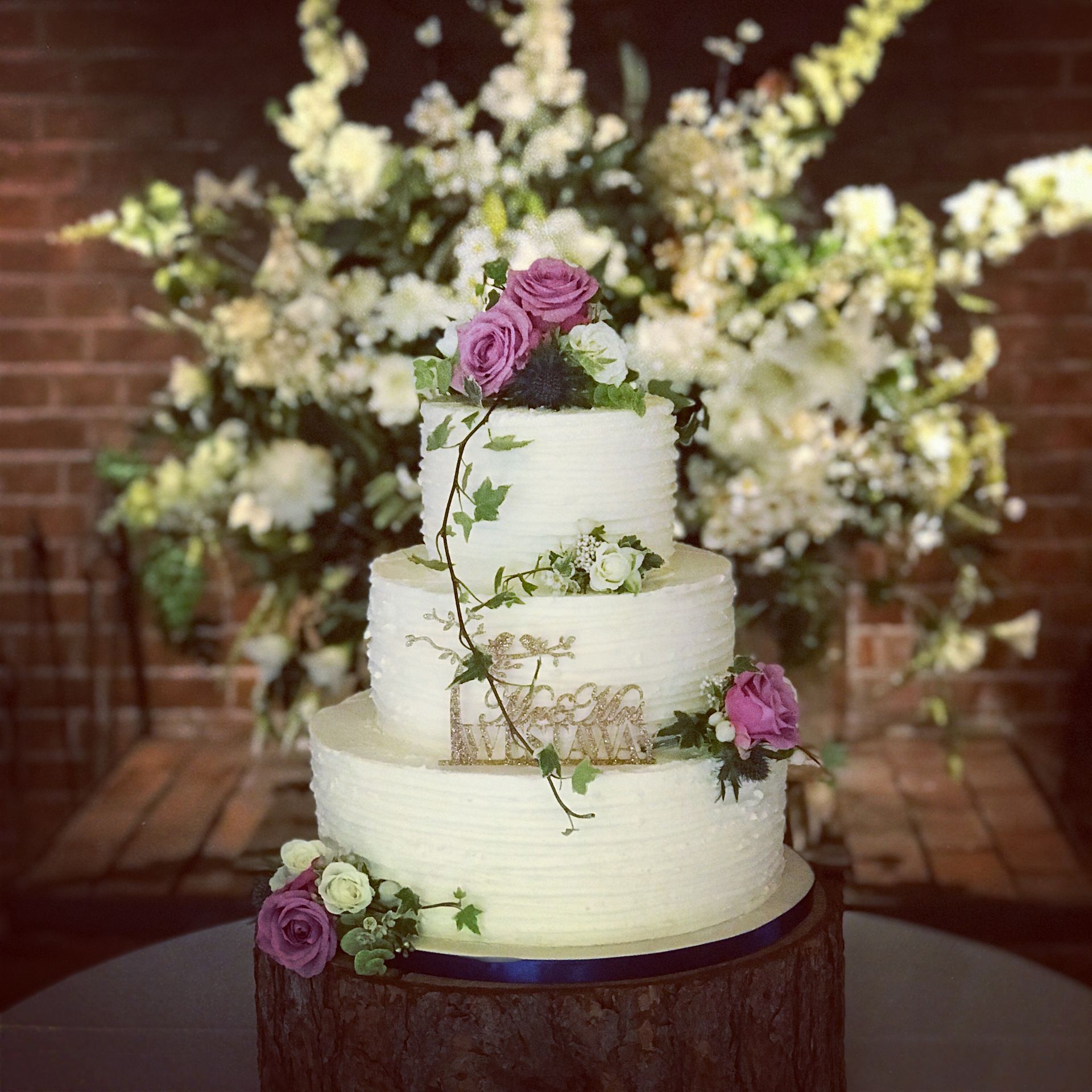 A wedding cake is sitting on top of a wooden stump surrounded by flowers.