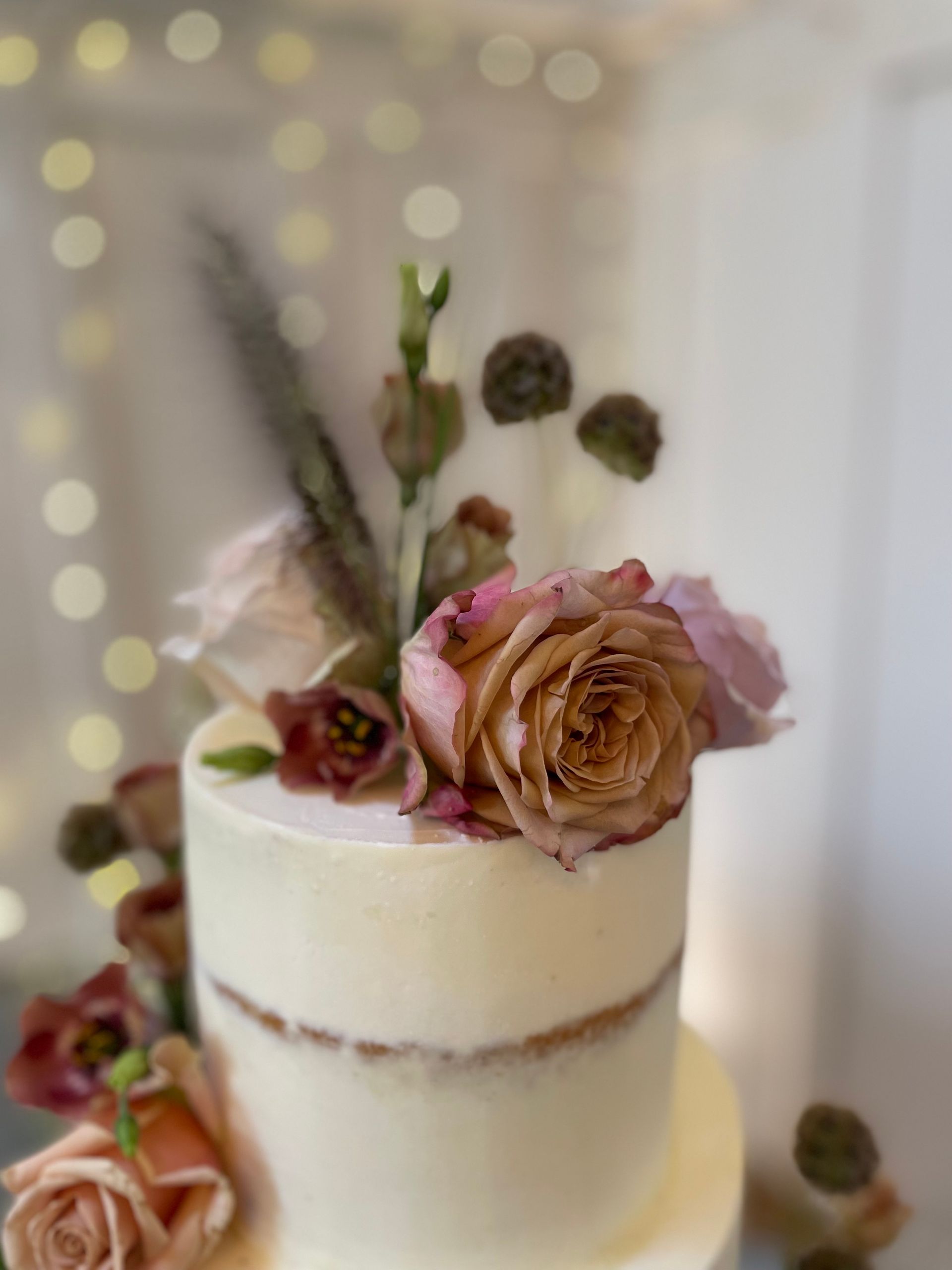 A wedding cake with roses and feathers on top