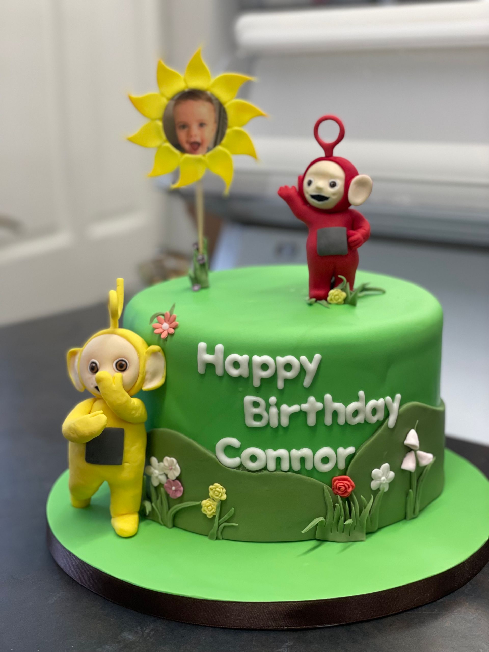A birthday cake for connor with teletubbies and a sunflower