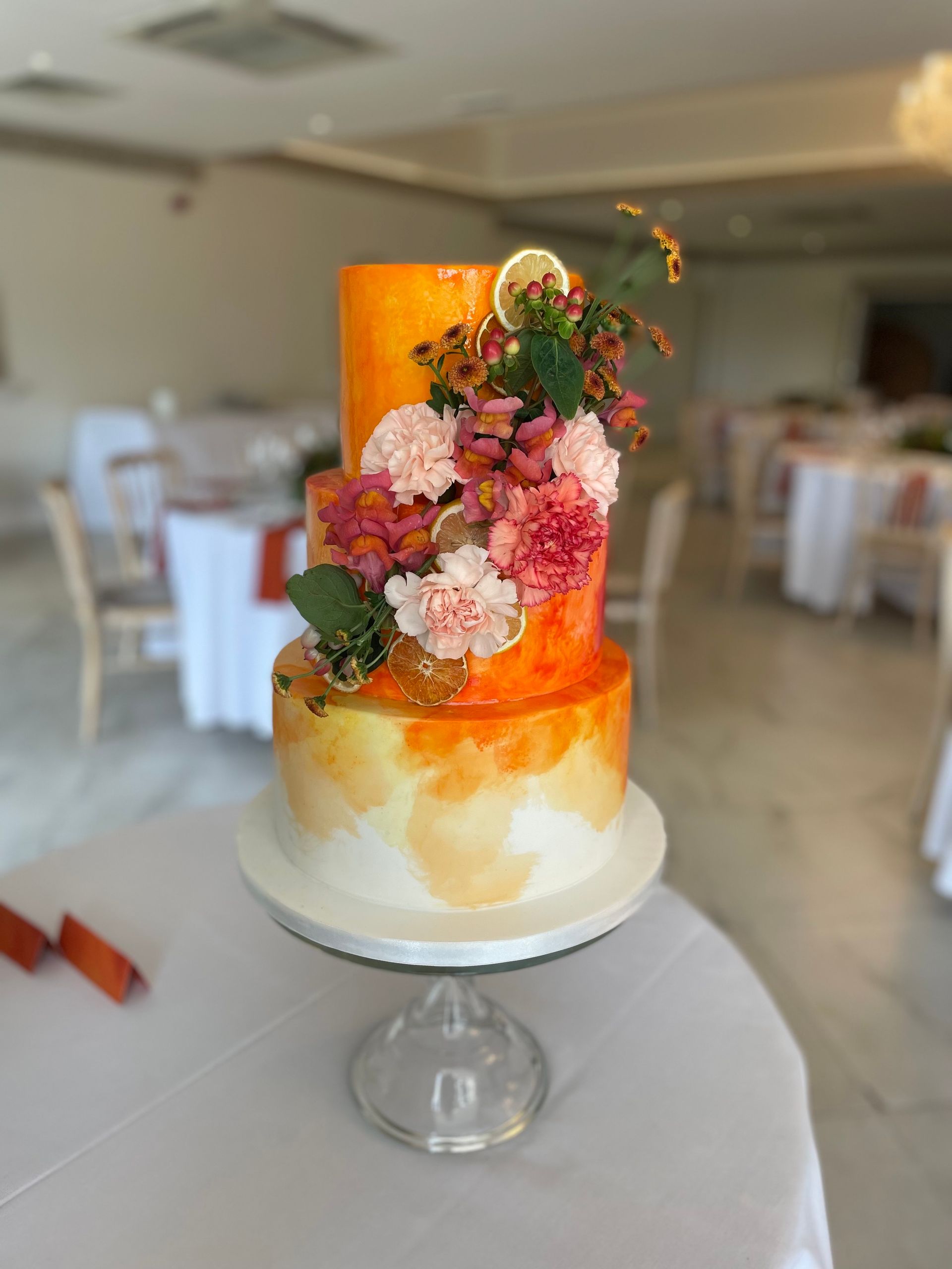 A three tiered cake with flowers on top of it is sitting on a table.