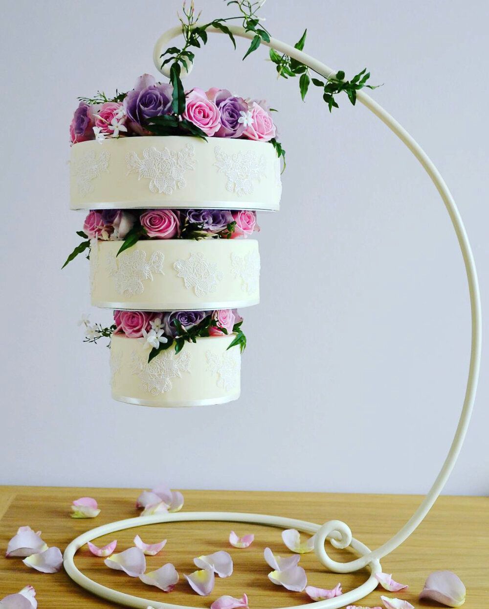 A wedding cake hanging from a metal stand with flowers on it