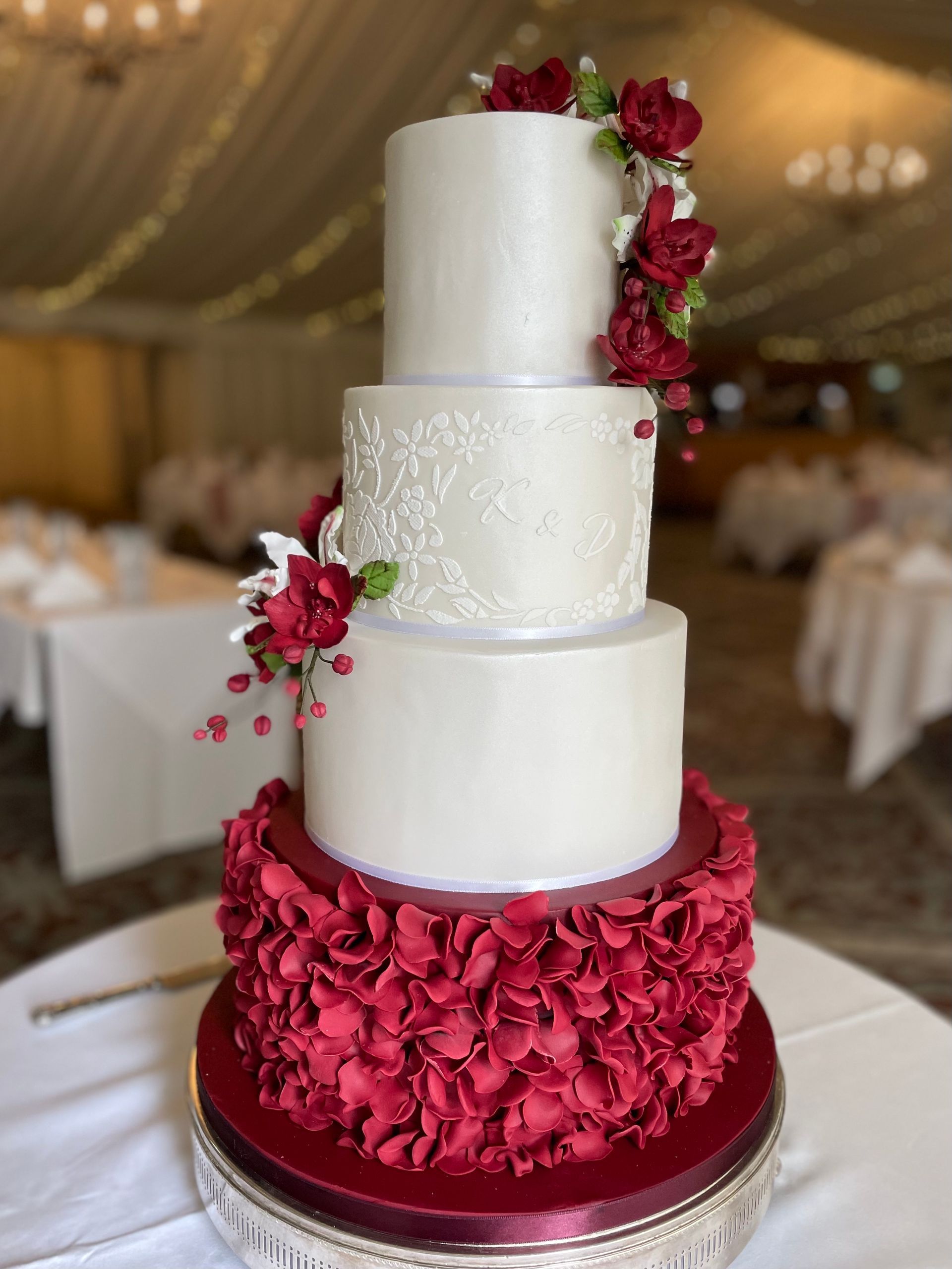 A white wedding cake with red flowers on it is sitting on a table.