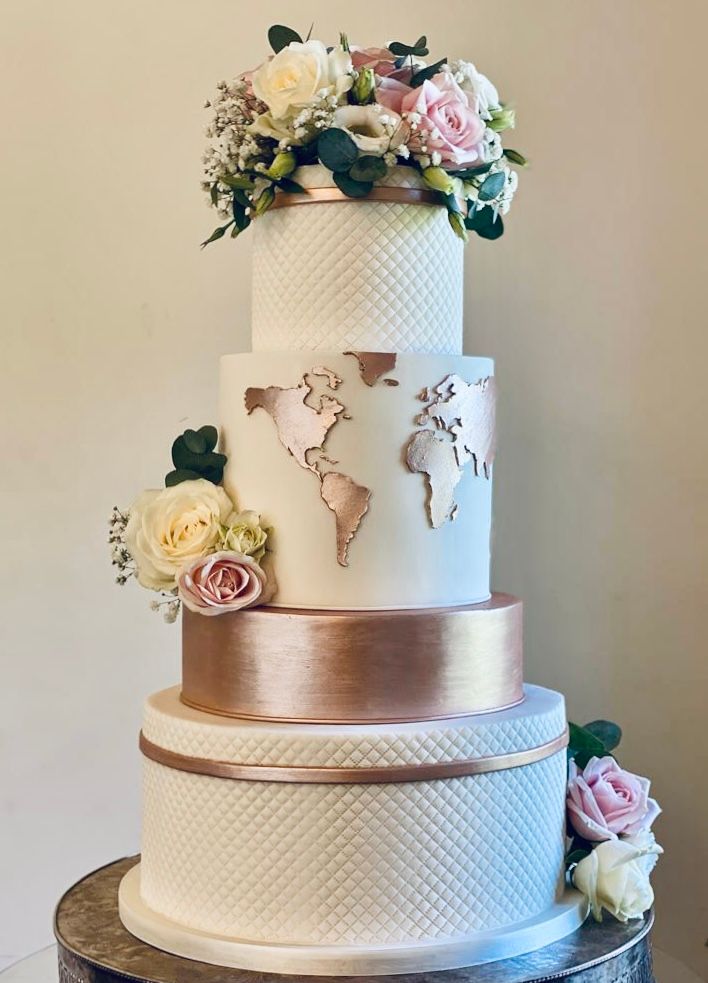 A wedding cake with a map of the world on it and flowers on top.