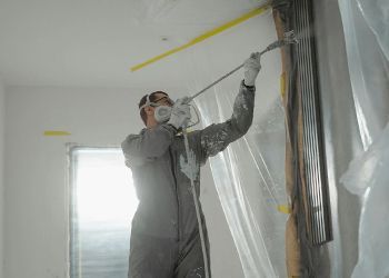 A man is painting a wall with a sprayer.