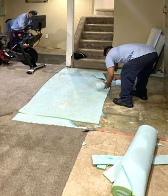 Two men are working on a carpet in a basement