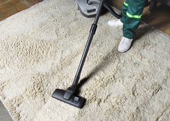 A person is using a vacuum cleaner to clean a rug.