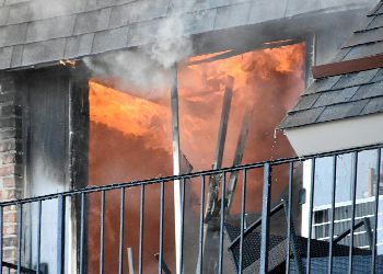 A fire is coming out of a window of a building.