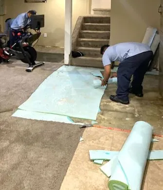 Two men are working on a carpeted floor in a basement.