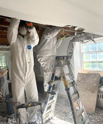 Two men in protective suits are working on a ceiling in a room.