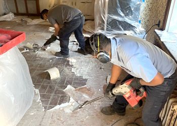 Two men are working on a tiled floor in a room.