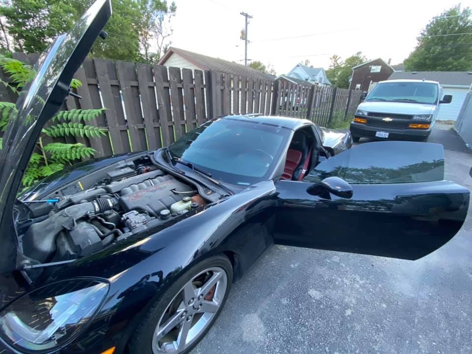 A black sports car with its hood up and its doors open