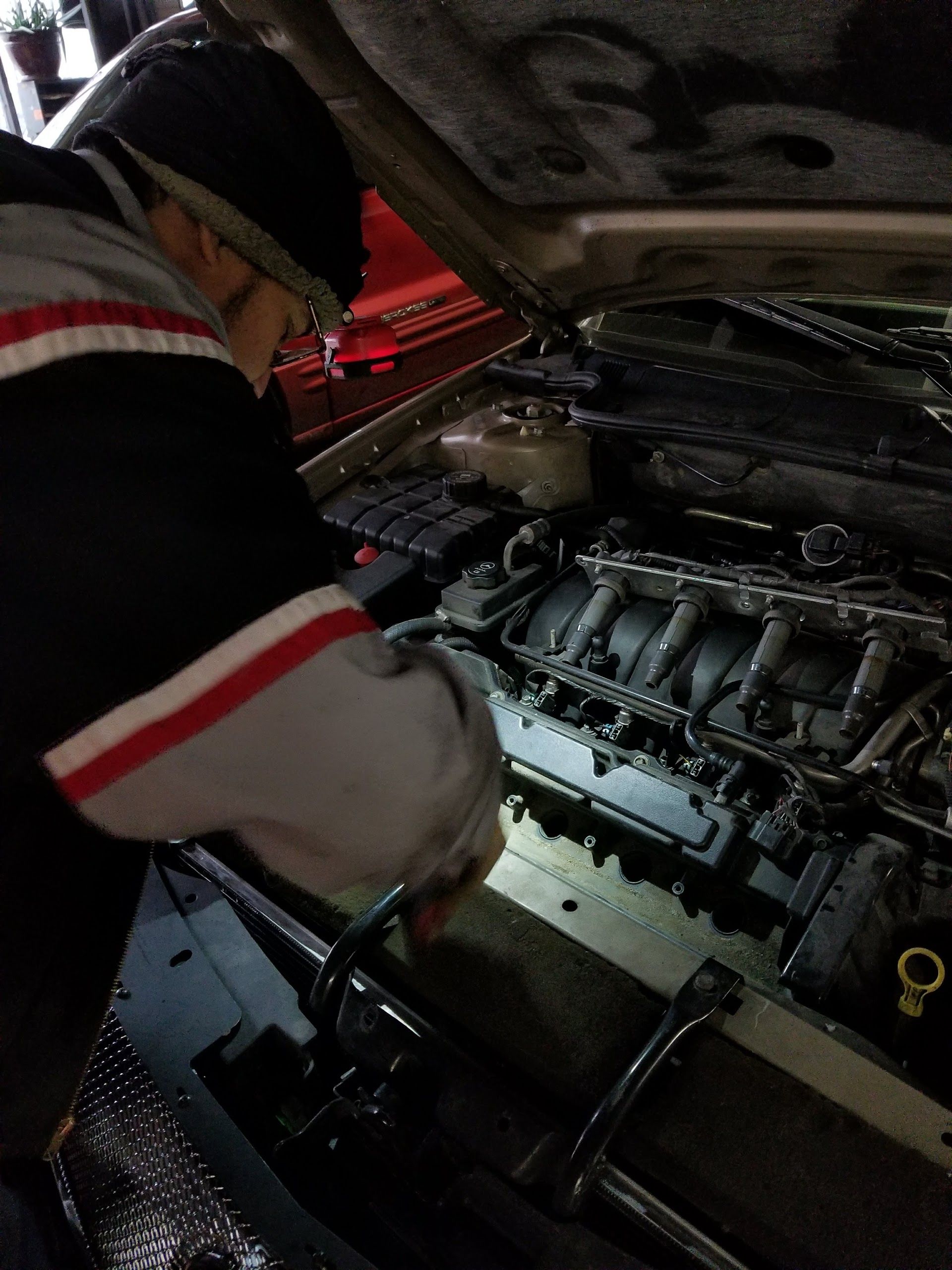Mechanic inspecting car engine under the hood, wearing dark clothes with red and white sleeves | G&R Auto Corp