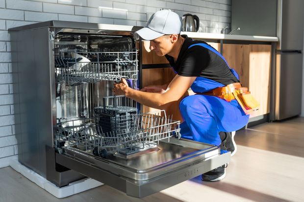 Worker loading dishes into an open dishwasher in a kitchen