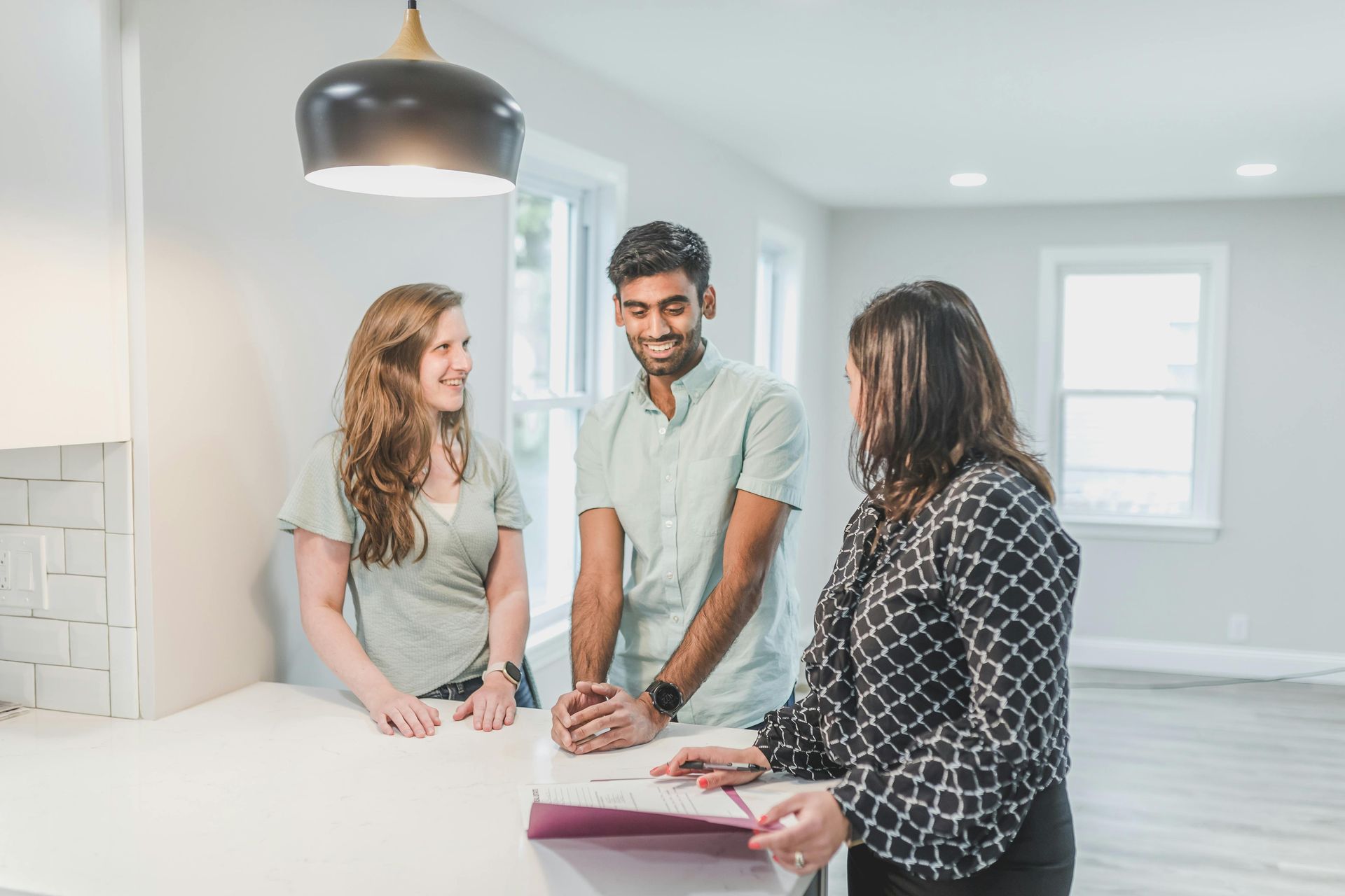 Three people discussing paperwork at a bright kitchen island