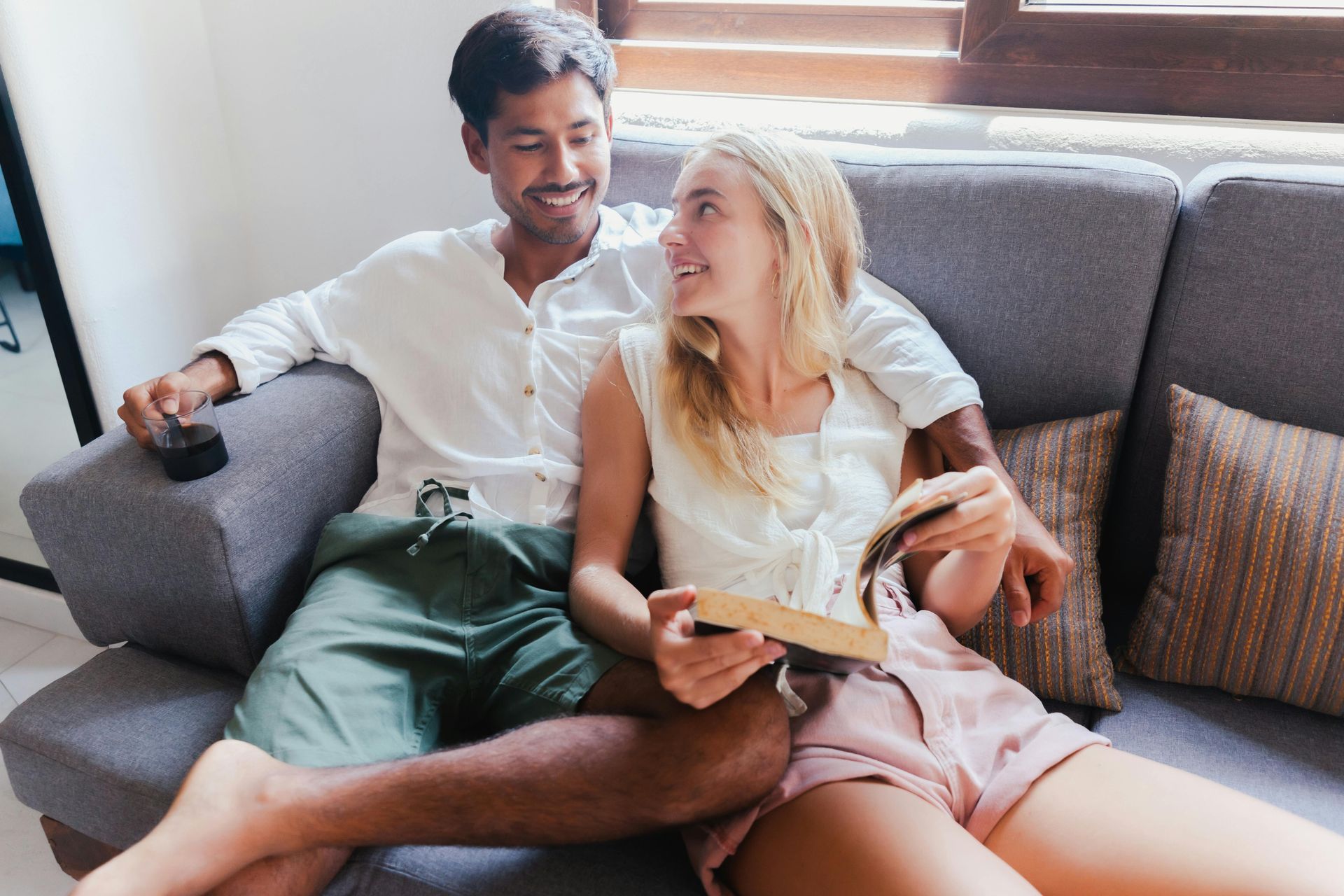 Two people sitting on a couch, smiling and reading a book together