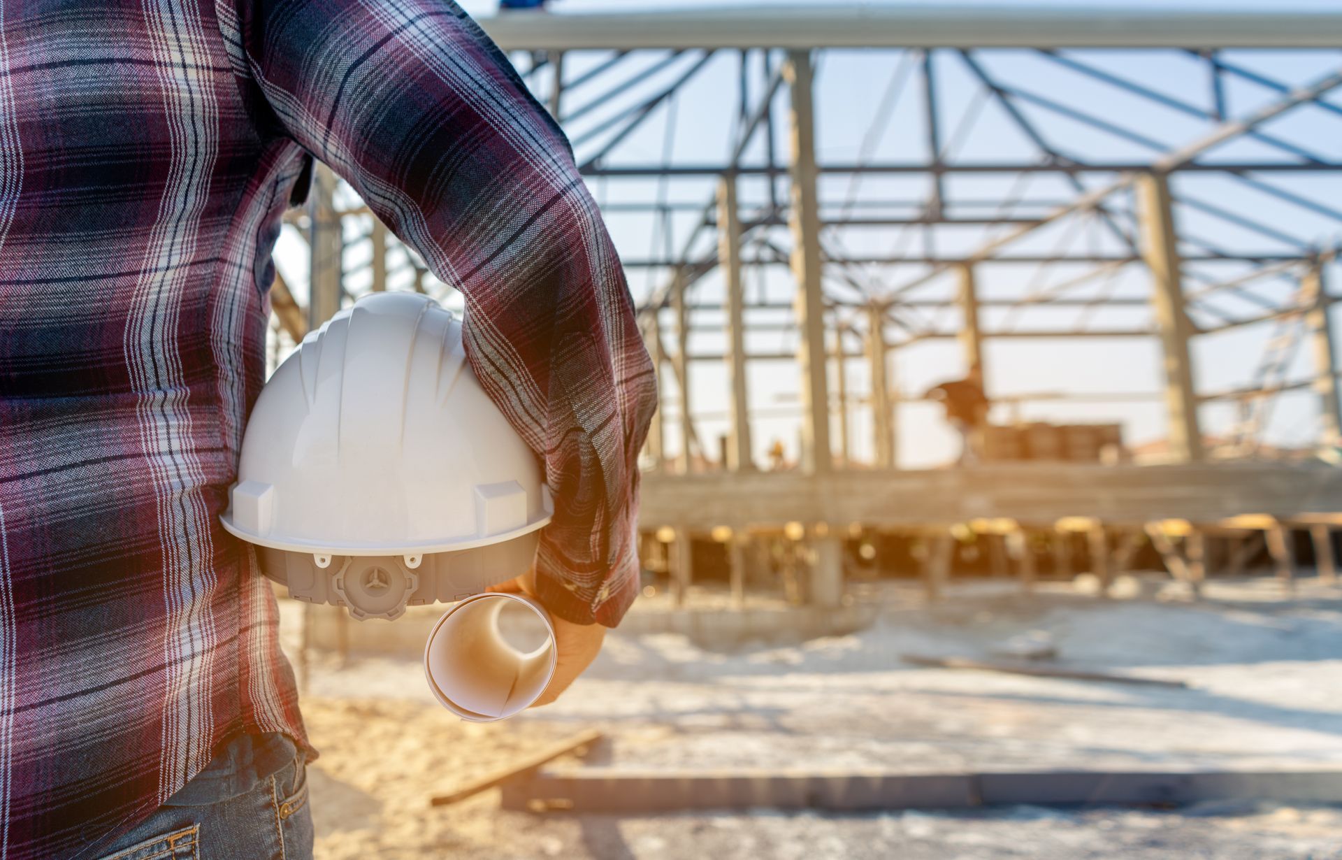 Construction worker holding a hard hat, standing in front of a building frame.