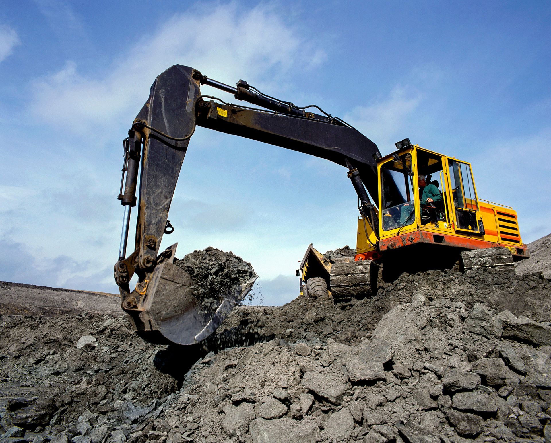 Yellow excavator digging into dark earth under a cloudy sky.