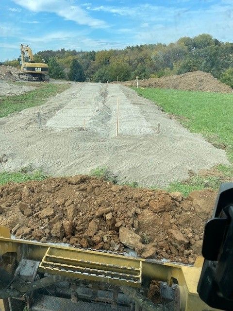 Yellow excavator on a dirt mound, scooping earth under a blue sky.