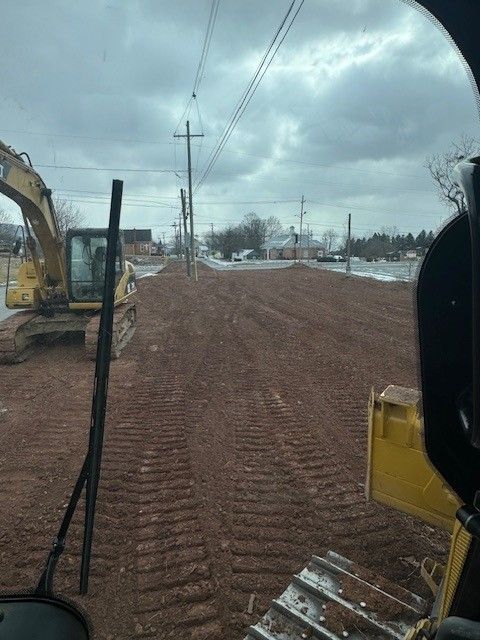 View from a machine cab of a construction site. Dirt road with excavator. Cloudy sky.
