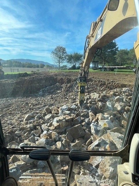 Excavator in action, breaking up rocks in a construction site with a blue sky overhead.