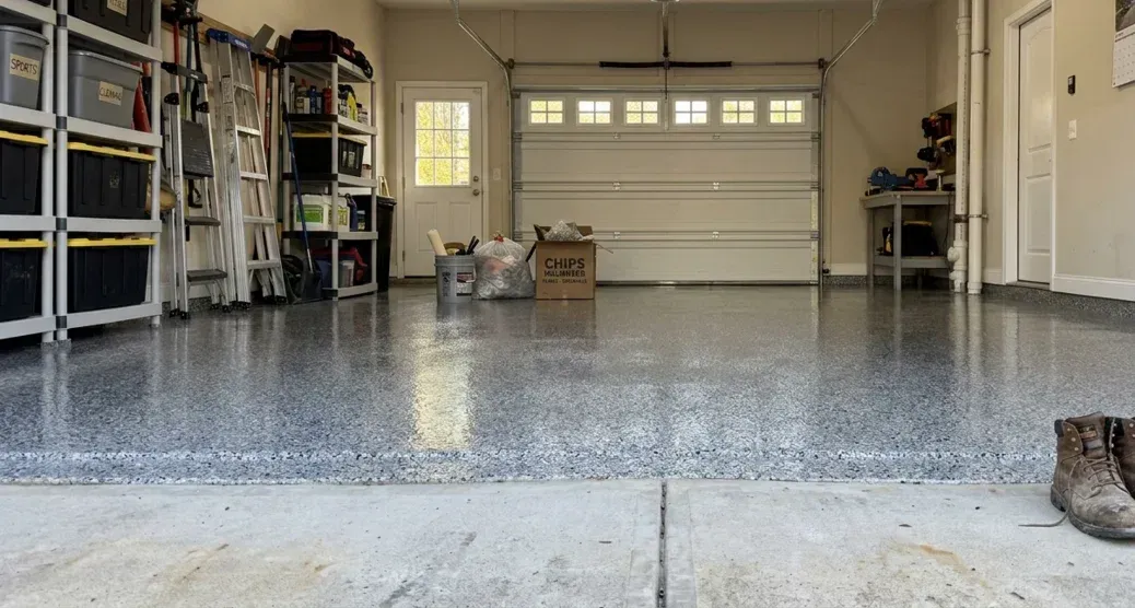 A clean, organized garage with a shiny gray epoxy-flecked floor, storage shelving, and a white garage door.