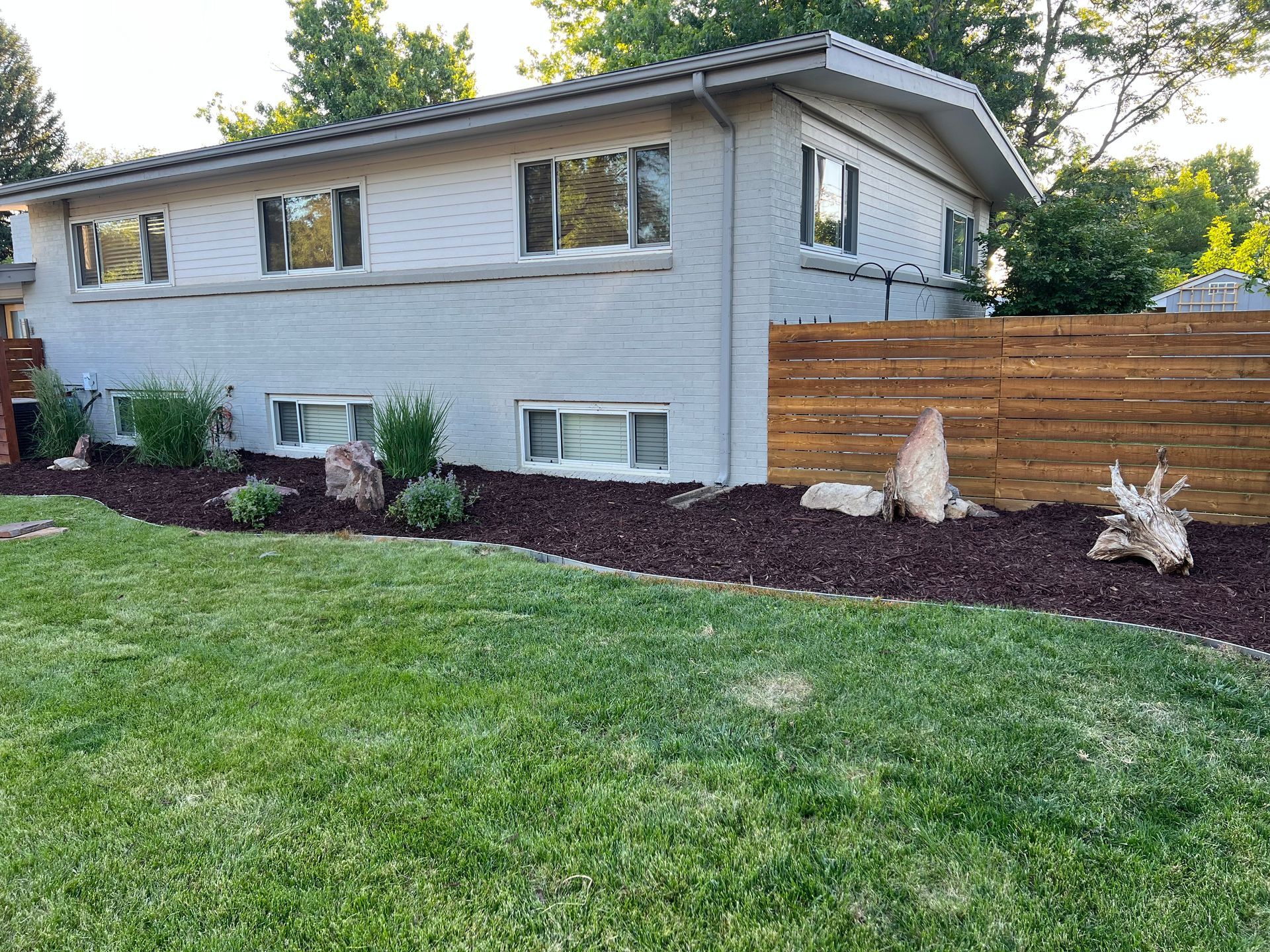Light blue brick house with a brown mulch bed and green lawn.