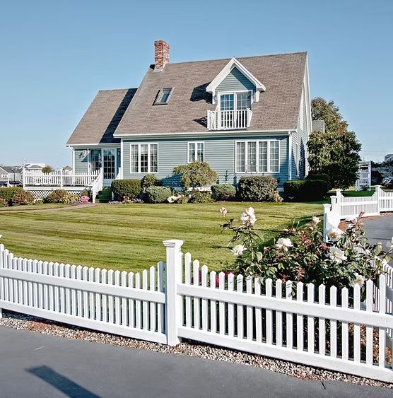 Blue house with white picket fence and well-kept lawn under a clear sky.