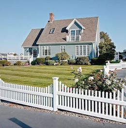 Blue house with white picket fence and well-kept lawn under a clear sky.
